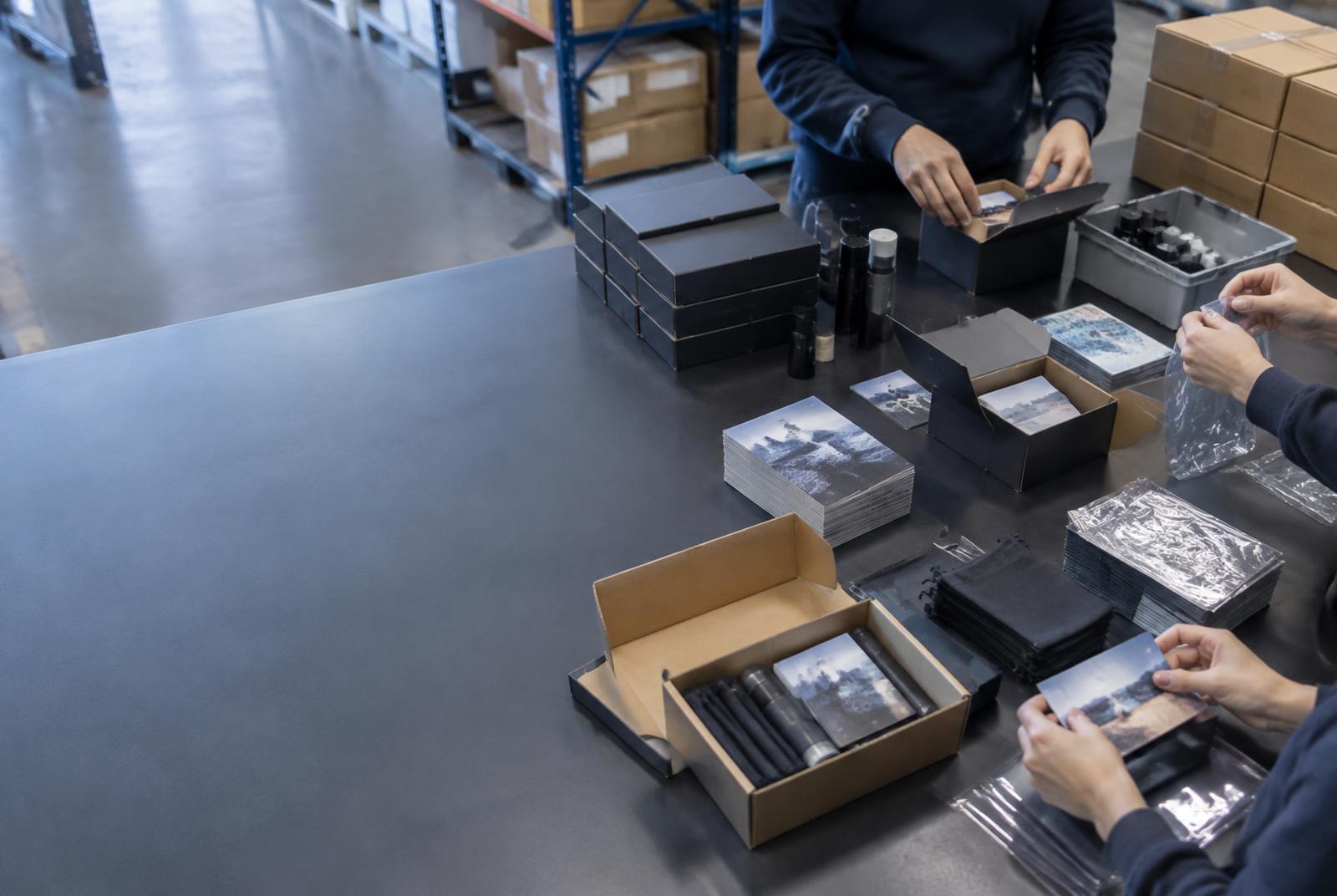 Mehrere Hände stellen an einem Arbeitstisch Produkte zu fertigen Verkaufseinheiten zusammen